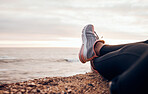 Fitness, shoes and sea in nature feeling relax with freedom outdoor sitting. Waves, ocean and water with a person and athlete taking a break from training and workout with feet in summer sun
