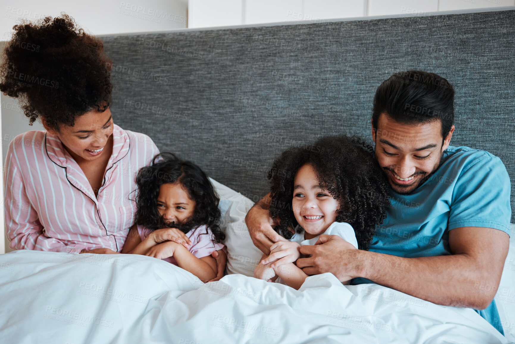 Buy stock photo Love, bonding and children laying with their parents in their bedroom playing, tickling and laughing. Happy, smile and girl kids being playful and relaxing with their mother and father in the bedroom