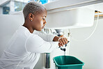 Plumbing, leak and time with a black woman in the bathroom of her home waiting for repair assistance. Sink, emergency and watch with a young female homeowner in her house to stop water using a bucket