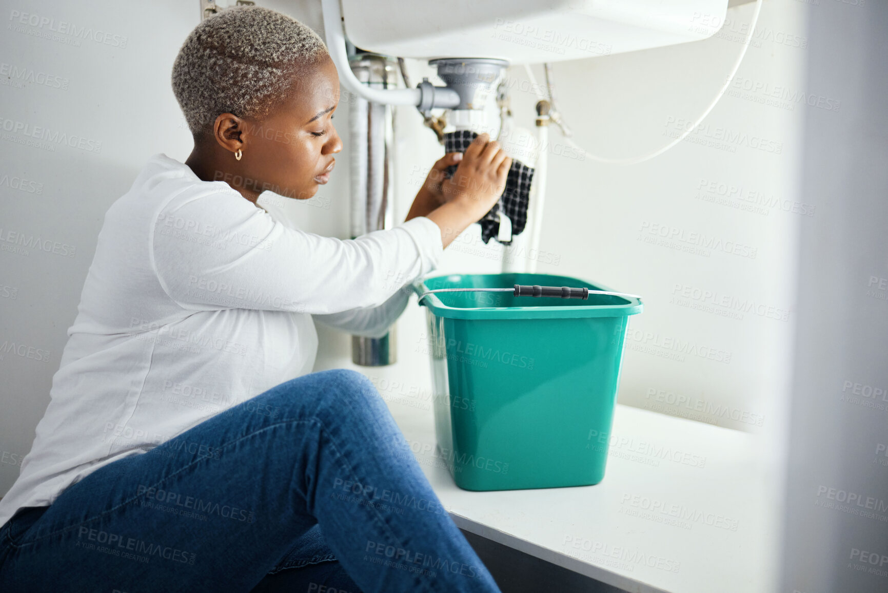 Buy stock photo Plumbing, leak and a black woman in the bathroom of her home with a cloth and bucket waiting for assistance. Sink, emergency and a burst pipe with a young female homeowner in her house to stop water