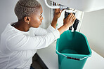 Plumbing, water and a black woman in the bathroom of her home with a cloth and bucket waiting for assistance. Sink, emergency and burst pipe with a young female homeowner in her house to stop a leak