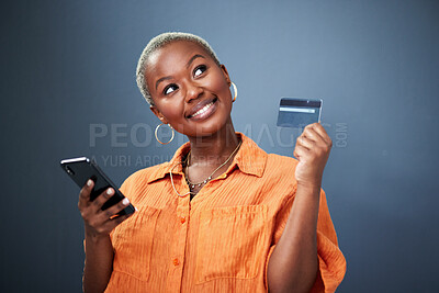 Buy stock photo Thinking, phone and credit card with a black woman online shopping in studio on a gray background. Mobile, ecommerce and finance payment with a young female shopper searching for a deal or sale