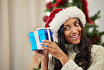 Christmas, curious or happy woman with a gift or box in present on a holiday celebration at home. Guessing, smile or excited Indian girl with present with giveaway prize package in a house in winter