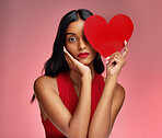 Woman, paper heart and face in studio portrait for makeup, beauty or romantic sign by red background. Girl, fashion model and cardboard emoji with love for cosmetic, valentines day date and aesthetic