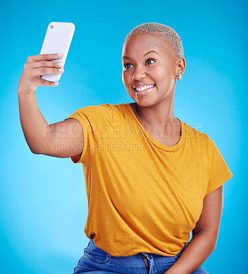 Buy stock photo Phone, selfie and smile with a black woman on a blue background in studio to update her status. Mobile, social media and a happy young female influencer taking a photograph for online profile