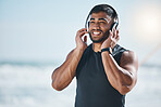 Music, headphones and happy man at the beach after fitness routine with podcast on blurred background. Radio, wellness and Indian male runner walking along the ocean after sports, training or workout