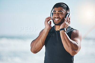 Buy stock photo Music, headphones and happy man at the beach after fitness routine with podcast on mockup space. Radio, wellness and Indian male runner walking along the ocean after sports, training or workout