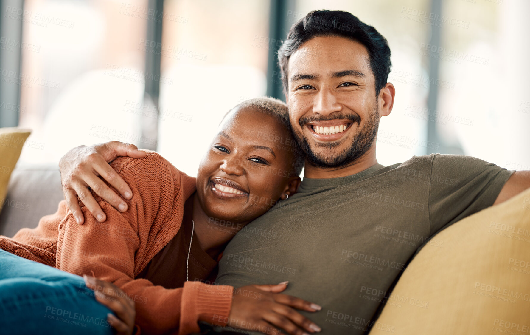 Buy stock photo Happy hug, interracial couple and portrait on a sofa at home with love and care in a living room. Woman, young people and together in a house sitting on a lounge couch relax with support and embrace