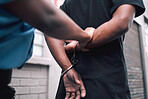 Hands, handcuffs or arrest with a police officer and criminal walking outdoor in a city from the back. Security, law or legal with a person of authority catching a crime suspect in an urban town