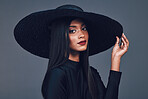 Face, fashion and serious woman with hat in studio isolated on a gray background. Portrait, style and confident female model from India with makeup cosmetics, classy clothes and elegant aesthetic.