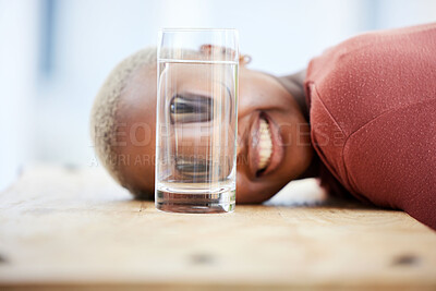 Buy stock photo Woman, funny face and water glass with big eyes, laughing and comic joke on table in apartment. African girl, crazy young student and comedy for meme with happy smile, home and playing game on desk