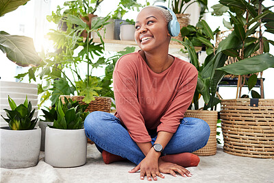 Buy stock photo Music, relax and thinking with a black woman in her home by plants while streaming an audio playlist. Headphones, radio and subscription service with a happy young female person in her house