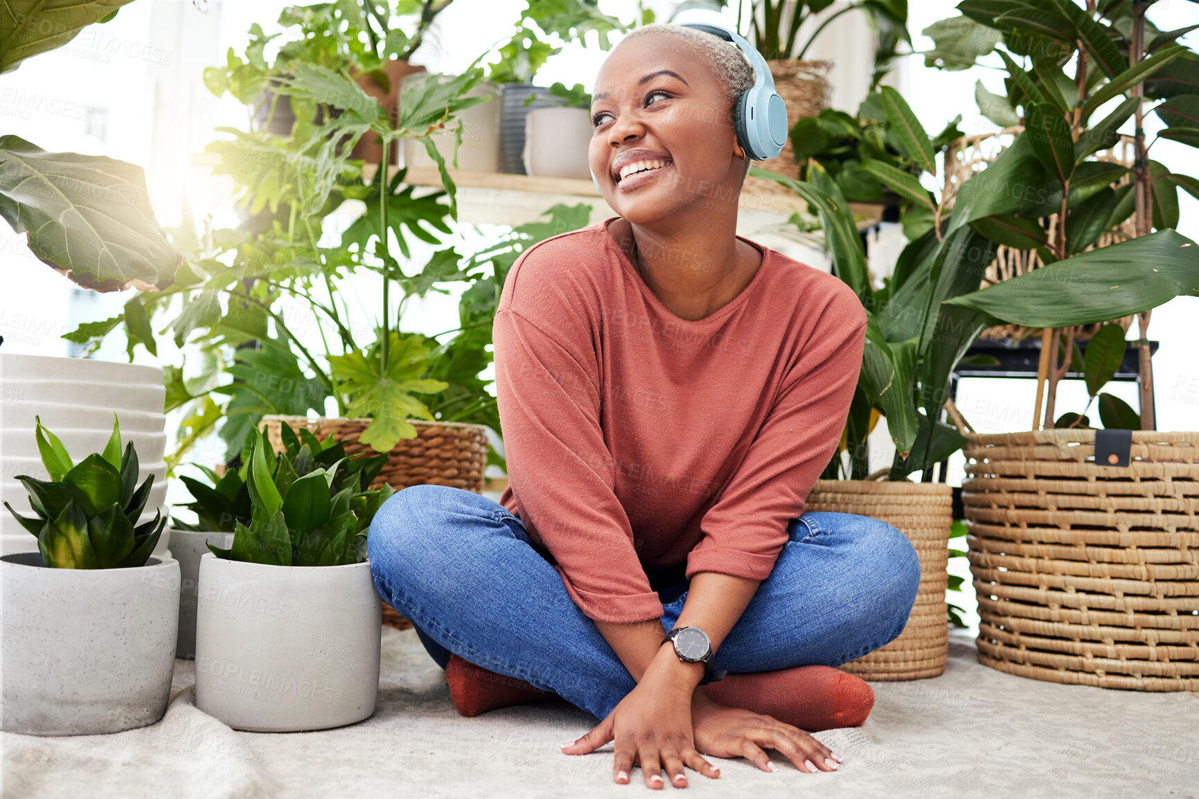 Buy stock photo Music, relax and thinking with a black woman in her home by plants while streaming an audio playlist. Headphones, radio and subscription service with a happy young female person in her house