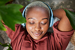 Woman, face and headphones for listening to music to relax on a floor with plants for peace and calm. Headshot of a black female person meditate with sound, audio and podcast or radio at home
