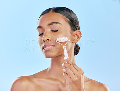 Buy stock photo Facial massage, woman and roller, beauty and skincare, natural cosmetics and tools isolated on blue background. Rose quartz, crystal and skin glow, Indian female model with dermatology and antiaging