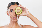 Woman, avocado and funny studio portrait for health, wellness and diet for facial glow by white background. Girl, model and fruit for skincare, nutrition or cosmetics with comic expression for beauty