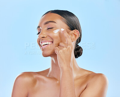 Buy stock photo Face cream, skin and beauty of a happy woman with natural glow on a blue background. Dermatology, moisturizer and cosmetics of an Indian female model for facial shine, wellness or self care in studio