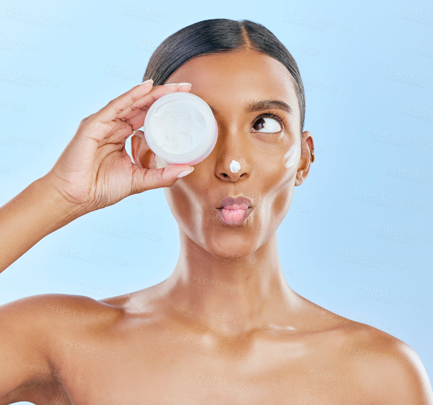 Buy stock photo Woman, face and cream jar in studio, blue background and cosmetics with kiss emoji. Indian female model, facial expression and beauty lotion in container for glow, skincare results and makeup product