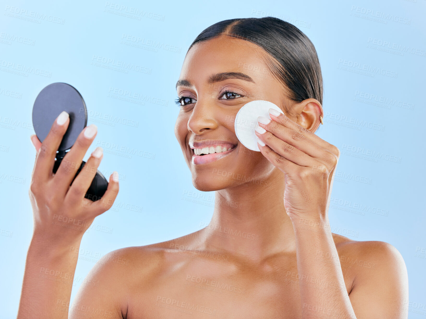 Buy stock photo Happy woman, cotton pad and skincare with mirror for makeup removal against a blue studio background. Female person with smile for beauty cosmetics, pamper or removing foundation in facial treatment