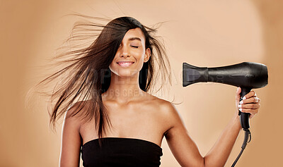Buy stock photo Hair, dryer and smile of woman in studio for beauty, grooming and heat equipment on background. Indian female model, haircare and tools with wind for hairstyle, salon appliance or aesthetic treatment