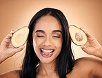Face, tongue out and woman with avocado for skincare isolated on a brown background in studio. Fruit, funny and happy model with food for nutrition, health or vegan diet, omega 3 or natural cosmetics