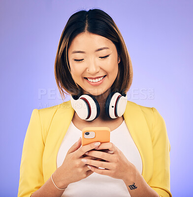 Buy stock photo Social media, phone and happy Asian woman in studio for text message, internet meme and chat. Headphones, smile and female person on smartphone listen to audio, song and track on purple background