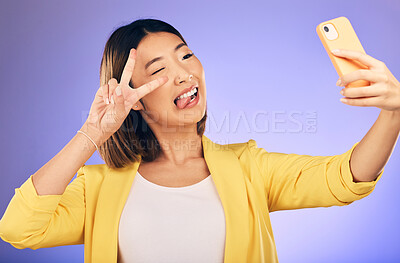 Buy stock photo Asian woman, peace sign and funny face for selfie, photo or memory against a purple studio background. Happy female person or model pose with peaceful emoji, goofy or silly for picture or online vlog