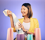 Shopping bag, clothes and woman or customer with product sale, discount or promotion on studio, purple background. Happy young model or asian person with fashion choice, retail and unboxing gift