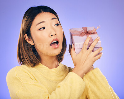 Buy stock photo Surprise, gift and box with face of asian woman in studio for birthday, celebration and curious. Thinking, wow and party with female person and present on purple background for giveaway and package