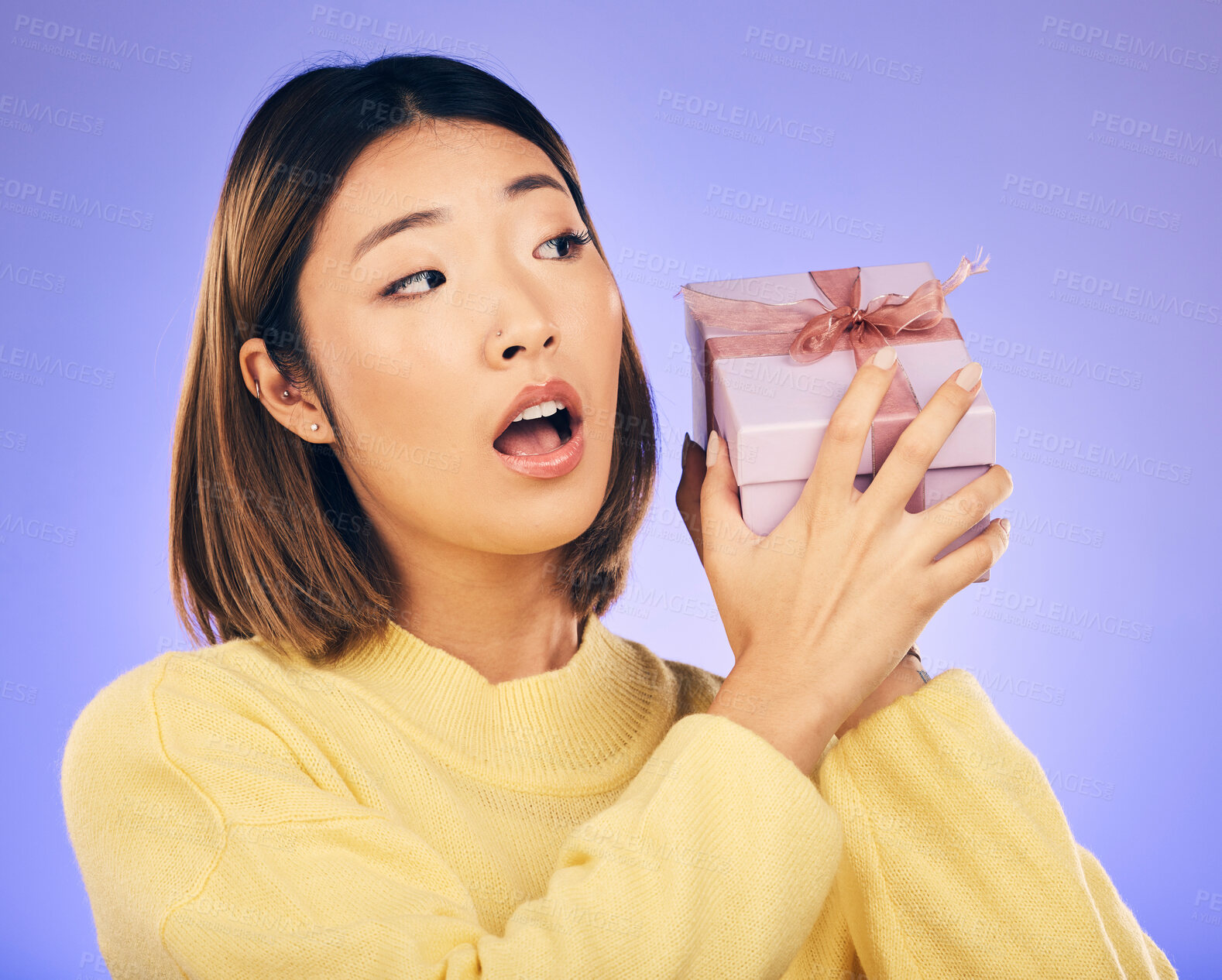 Buy stock photo Surprise, gift and box with face of asian woman in studio for birthday, celebration and curious. Thinking, wow and party with female person and present on purple background for giveaway and package