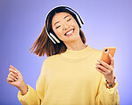 Dance, music and happy Asian woman with phone in studio for streaming, subscription and radio. Relax, headphones and female person on smartphone listen to audio, song and track on purple background