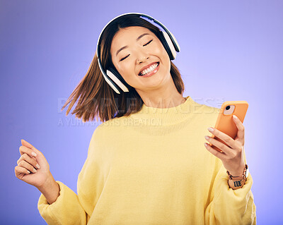 Buy stock photo Dance, music and happy Asian woman with phone in studio for streaming, subscription and radio. Relax, headphones and female person on smartphone listen to audio, song and track on purple background
