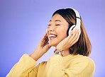 Happy asian woman, headphones and listening to music for online streaming against a purple studio background. Female person or model smile enjoying audio track, sound or songs on headset on mockup