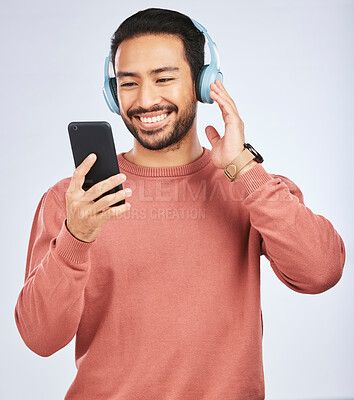 Buy stock photo Man, headphones and smartphone for music in studio, white background and podcast app. Happy asian male model, cellphone and listening to audio, streaming mobile sound and online radio media with tech