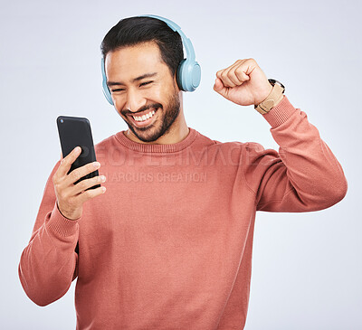 Buy stock photo Man, headphones and celebrate success with smartphone, music and white background in studio. Asian male model, cellphone and fist for happy dance, excited audio deal and hearing winning news on radio