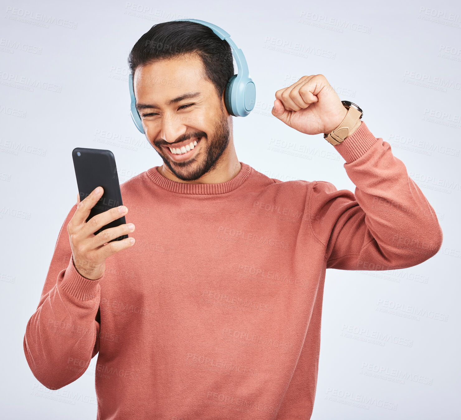 Buy stock photo Man, headphones and celebrate success with smartphone, music and white background in studio. Asian male model, cellphone and fist for happy dance, excited audio deal and hearing winning news on radio