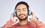 Man, headphones and calm music in studio, white background and podcast for peace. Face of happy young asian male model listening to audio, streaming sound and hearing radio to relax with song in mind