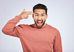 Portrait, angry and asian man with hand gun in studio for suicide, threat or shooting warning on grey background. Screaming, stress and face of male person with anxiety, self harm or bipolar crisis