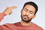 Depression, face and asian man with hand gun in studio for anxiety, trauma or ptsd on grey background. Finger, suicide and male sad with stress, anxiety or self harm, bipolar or mental health crisis