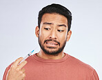 Fear, vaccine and face of asian man in studio with needle, phobia or covid scare on grey background. Corona, compliance and male person afraid of vaccination, medicine or prescription diabetic shot