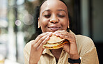 Restaurant, fast food and black woman eating a burger in an outdoor cafe as a lunch meal craving deal. Breakfast, sandwich and young female person or customer enjoying a tasty unhealthy snack