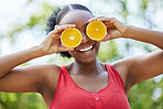 Happy black woman, vitamin C and orange on eyes for natural nutrition or citrus diet in nature outdoors. Portrait of African female person smile with organic fruit for health and wellness in the park