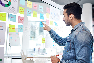 Buy stock photo Creative man, sticky note and pointing on glass board for schedule tasks, planning or brainstorming at office. Male person or employee with plan, agenda or marketing strategy for startup at workplace