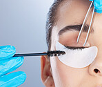 Woman, lashes and tweezer with mascara, studio closeup and makeup artist in gloves, hands and extension. Girl, model and zoom of face for beauty, cosmetics and brush for aesthetic by gray background