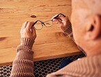Senior man, hand holding glasses and eye care with vision, prescription lens and designer frame at table. Elderly guy, hands and spectacles for vision, eyesight and health at desk in retirement home