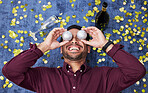 Christmas, drunk and funny with a man on the floor, laughing during a party or celebration event from above. Comic, comedy or festive with a happy young male person holding decorations over his face