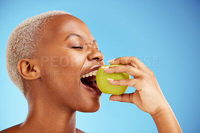 Buy stock photo Black woman, apple and bite in diet, nutrition or health and wellness against a blue studio background. Face of African female person eating natural organic fruit for vitamin, fiber or food on mockup