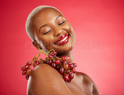 Buy stock photo Skincare, smile and grapes with a model black woman in studio on a red background for health or nutrition. Beauty, happy and fruit with a young female person posing for wellness, diet or detox