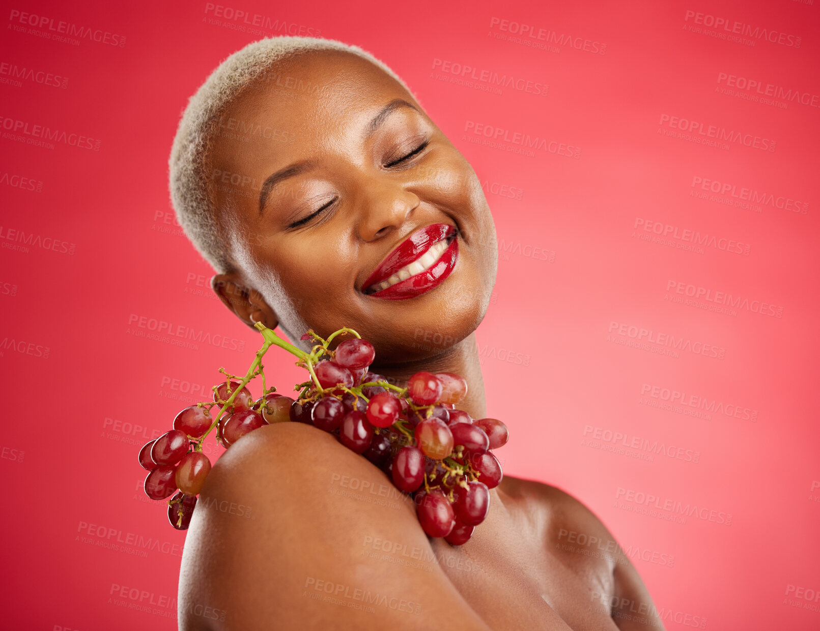 Buy stock photo Skincare, smile and grapes with a model black woman in studio on a red background for health or nutrition. Beauty, happy and fruit with a young female person posing for wellness, diet or detox