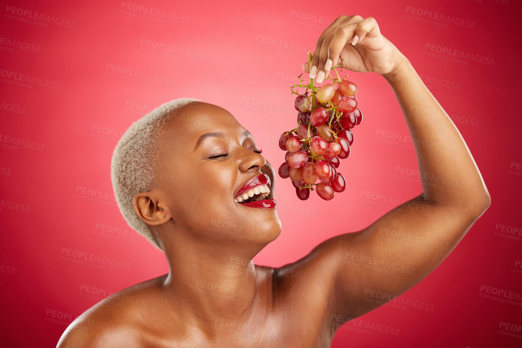 Buy stock photo Happy, eating and black woman with grapes on a red background for nutrition, diet or health. Smile, beauty and an African model or girl with fruit, hungry and food for a detox isolated on a backdrop